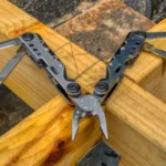 Ein vielseitiges Multi-Tool, das alle Werkzeuge, wie Messer, Säge und Zange, ausgeklappt auf einer Holz-Werkbank präsentiert.