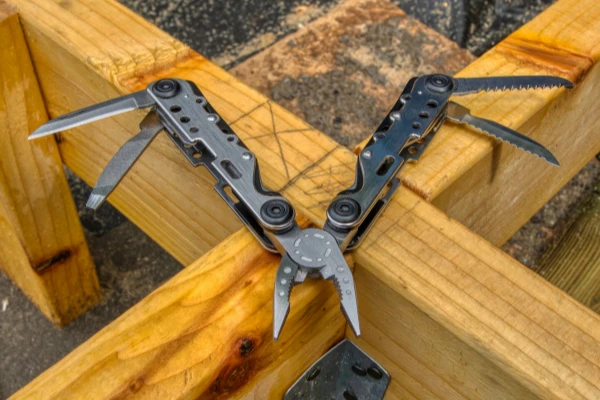 Ein vielseitiges Multi-Tool, das alle Werkzeuge, wie Messer, Säge und Zange, ausgeklappt auf einer Holz-Werkbank präsentiert.