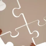 Nahaufnahme eines großen Puzzels, welches von mehreren Personen zusammengestellt wird.